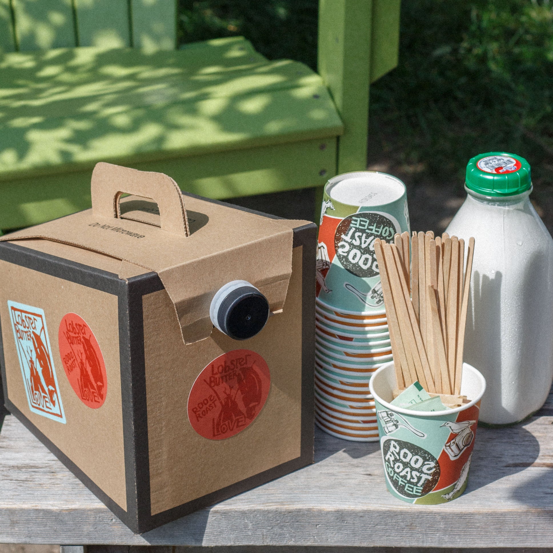 Cardboard box with a straw, cup, and bottle on a table outdoors.