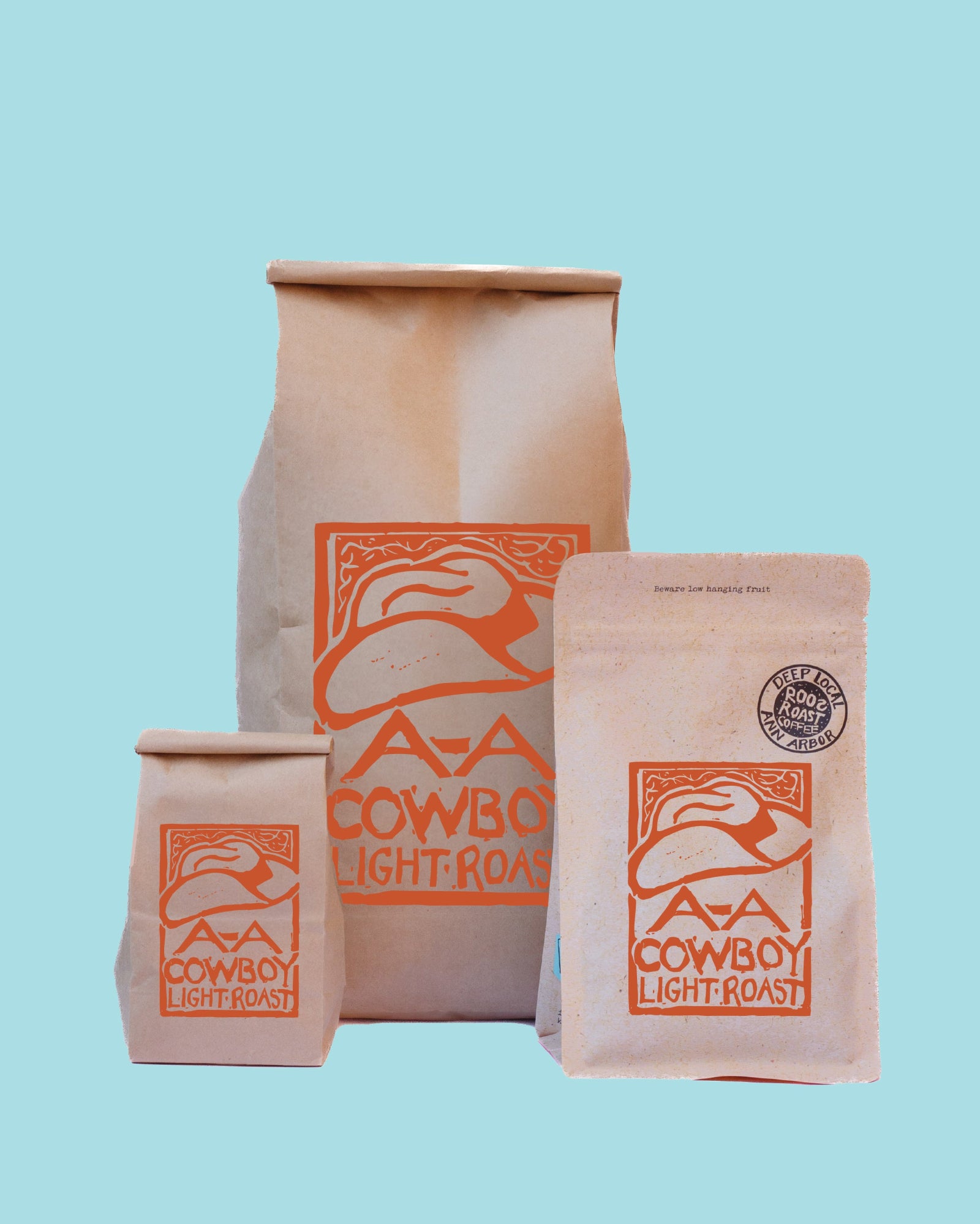 Three paper coffee bags of AAA Cowboy Light Roast in different sizes, arranged against a solid light blue background.