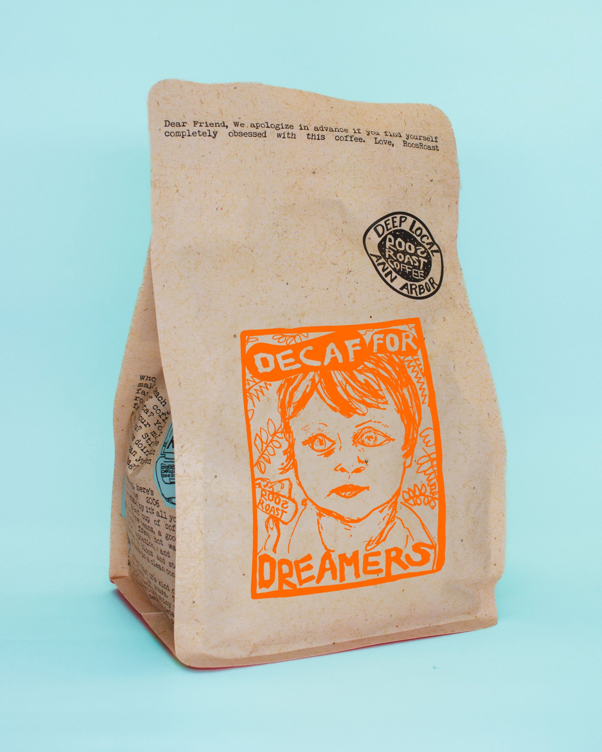 A stand-up kraft paper coffee bag on a light blue background. The bag has an orange graphic print reading 'DECAF FOR DREAMERS' with a stylized face illustration, a black circular seal that says 'DECAF COFFEE FROM THE ROOSTERS', and small printed text near the top.