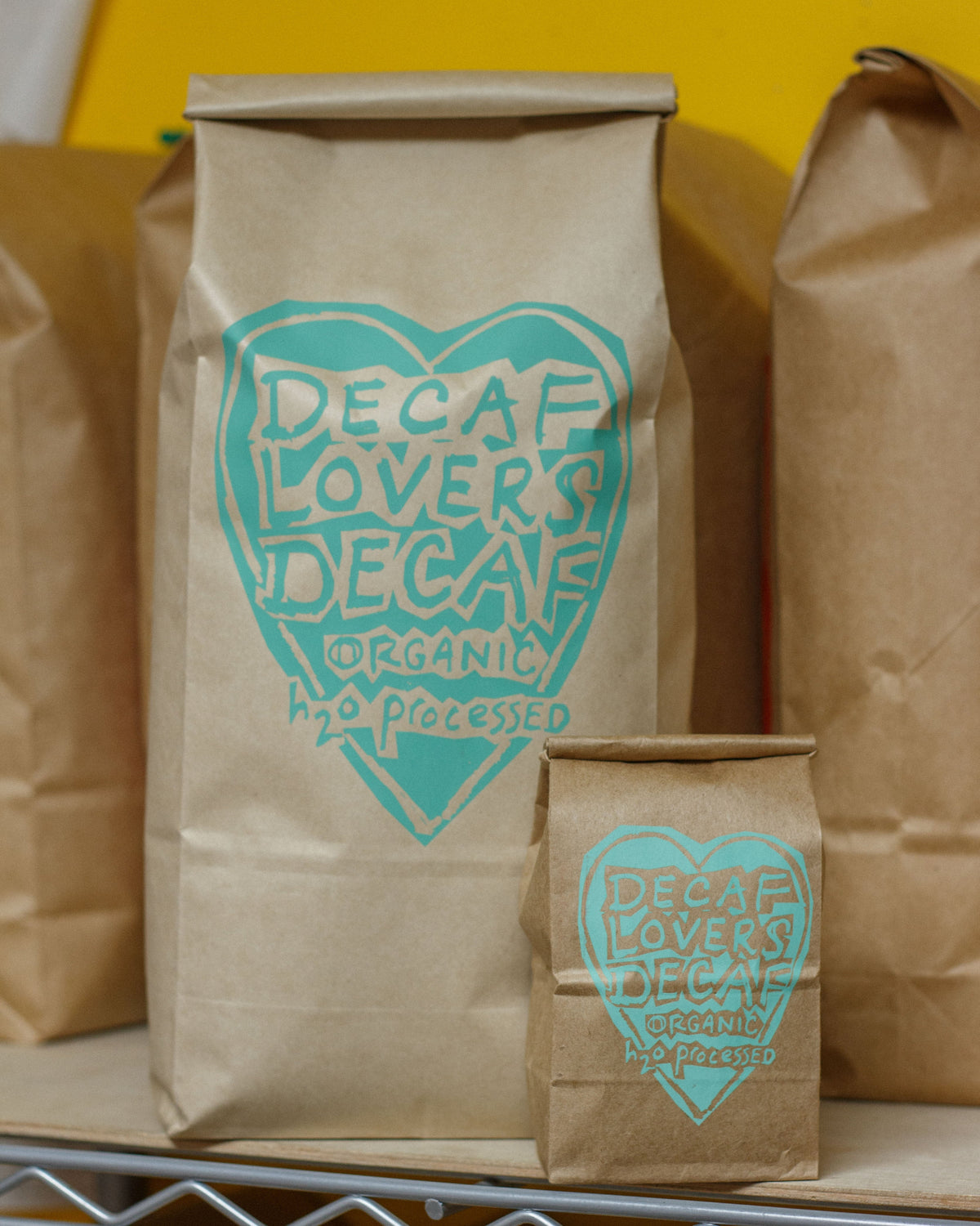 Brown paper bags with 'Decaf Lovers' logo on a yellow background