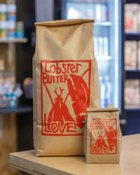 Two brown paper bags with red 'Lobster Butter Love' logo on a wooden surface.