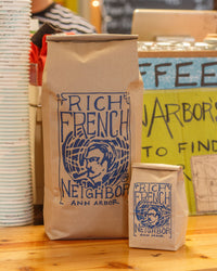 Two coffee bags labeled 'Rich French Neighbor' on a wooden surface with a colorful background.