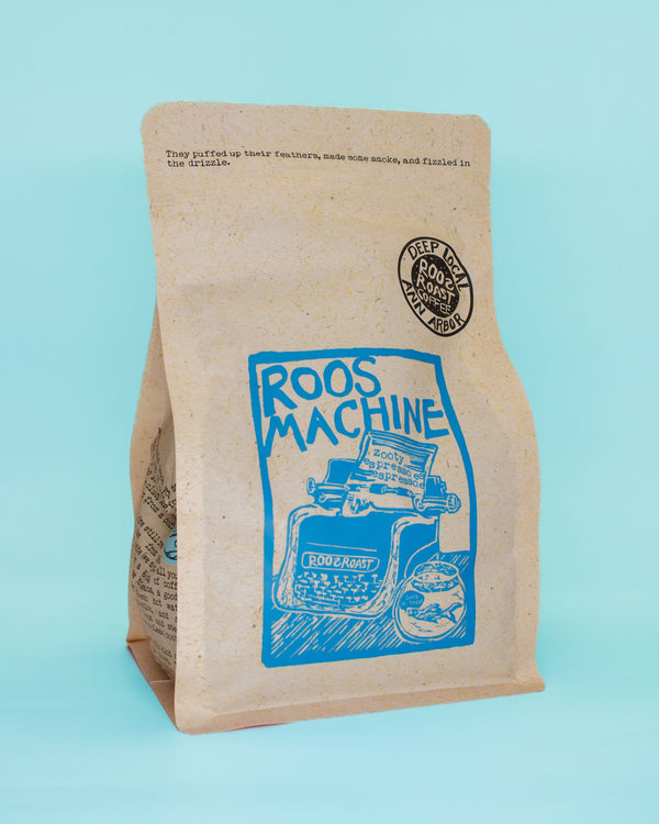 Kraft paper coffee bag with blue graphic and 'Roos Machine' text on a light blue background