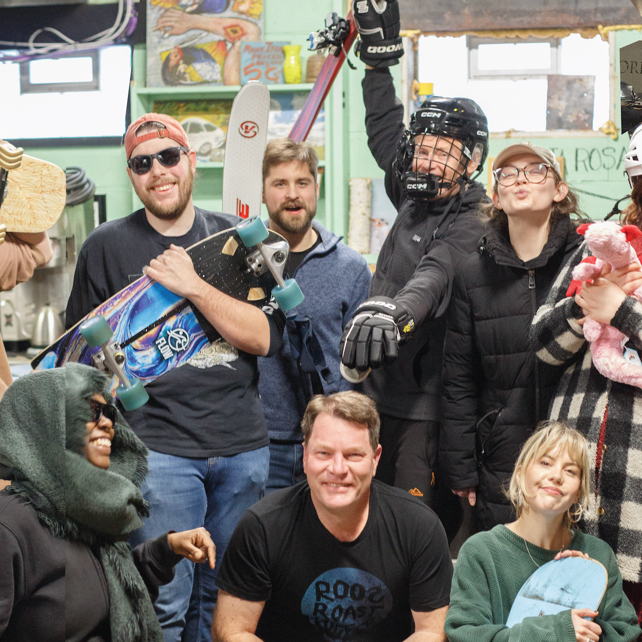 Group of people in a casual indoor setting with one person holding a helmet and skis.