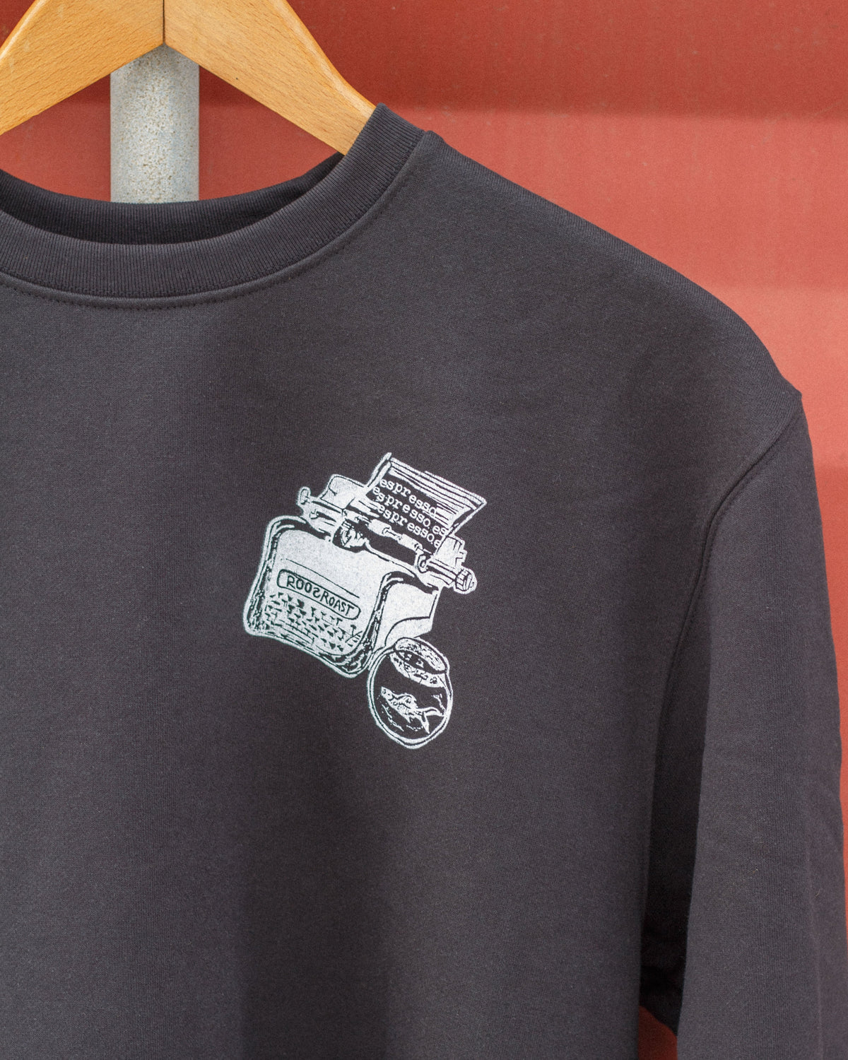 Black sweatshirt with a white typewriter graphic on a hanger against a red background