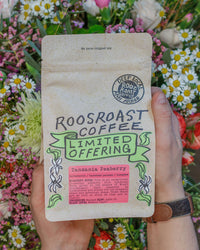 Hand holding a Roosroast Coffee package with flowers in the background