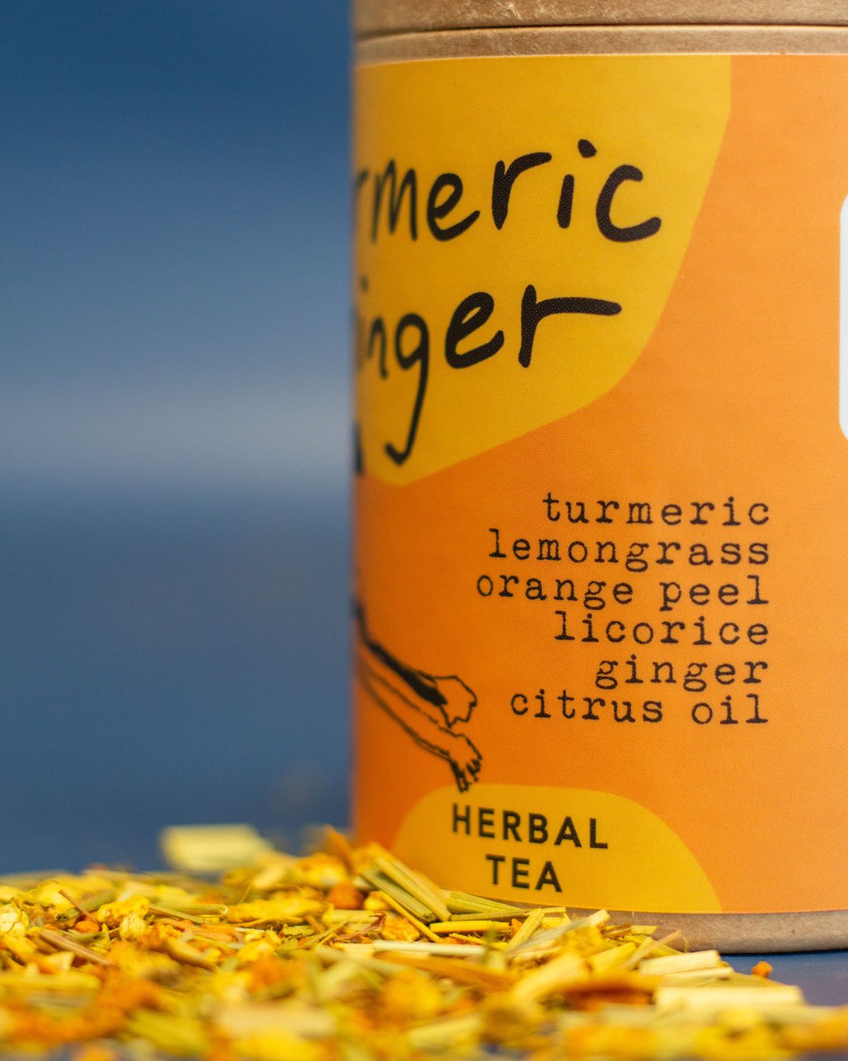 Tea canister labeled 'Turmeric Ginger' with tea leaves on a blurred natural background